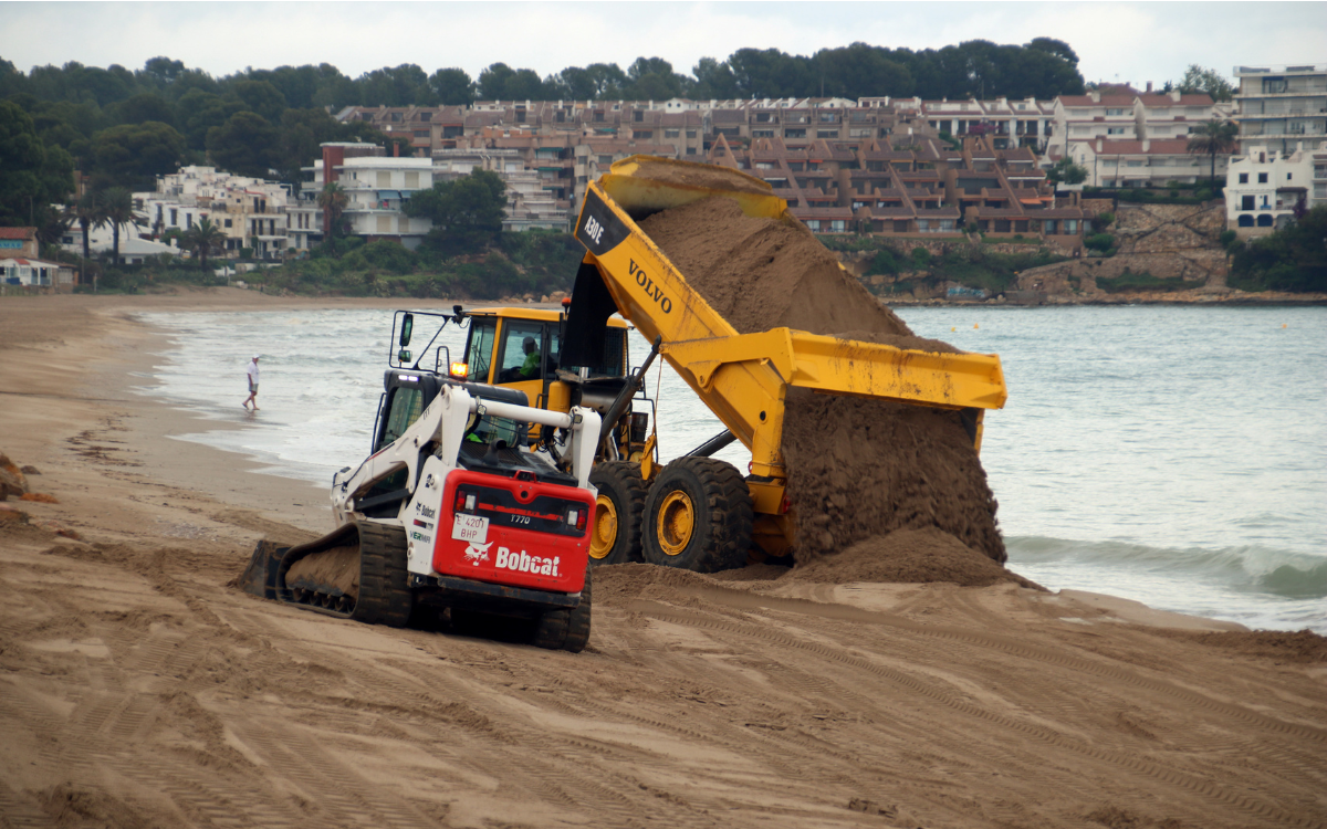 Un camió dipositant arena i una excavadora movent sorra a la platja d'Altafulla.